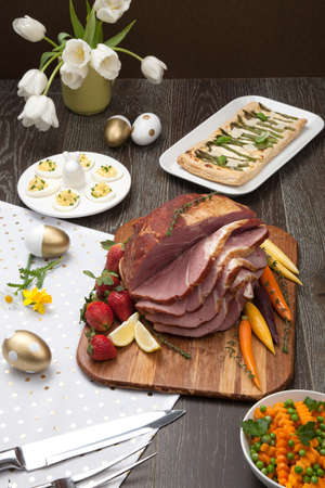 Delicious spicey roasted ham with deviled eggs, asparagus parmesan pastry, butternut squash with green peas, baby carrots, strawberries, and Easter decoration.の写真素材