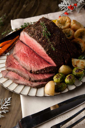 Uncut piece pf peppercorn roast beef with herbed Yorkshire puddings garnished with roasted vegetables.の写真素材
