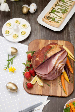 Delicious spicey roasted ham with deviled eggs, asparagus parmesan pastry, butternut squash with green peas, baby carrots, strawberries, and Easter decoration.の写真素材