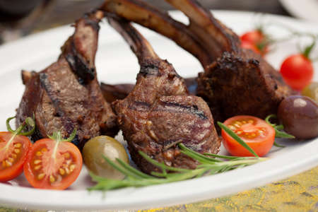 Grilled lamb chops served with cherry tomatoes and olives. Watermelon and wine. Outside dinner in a garden.の写真素材