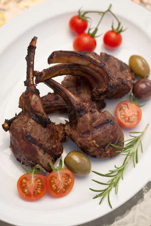 Grilled lamb chops served with cherry tomatoes and olives. Watermelon and wine. Outside dinner in a garden.の写真素材