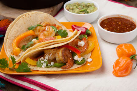 Two shrimp fajitas with bell pepper, onion, and jalapeno in a plate and shrimp fajitas in a cast iron skillet ready to be served. Guacamole, salsa, and tortillas.の写真素材