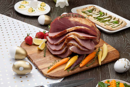 Delicious spicey roasted ham with deviled eggs, asparagus parmesan pastry, butternut squash with green peas, baby carrots, strawberries, and Easter decoration.の写真素材
