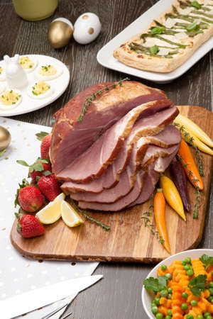 Delicious spicey roasted ham with deviled eggs, asparagus parmesan pastry, butternut squash with green peas, baby carrots, strawberries, and Easter decoration.の写真素材