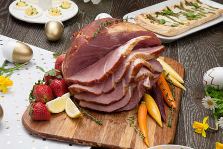 Delicious spicey roasted ham with deviled eggs, asparagus parmesan pastry, butternut squash with green peas, baby carrots, strawberries, and Easter decoration.の写真素材