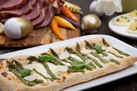 Asparagus parmesan puff pastry sidedish for delicious spicey roasted Easter ham dish, deviled eggs, butternut squash with green peas, baby carrots, strawberries, and Easter decoration.の写真素材