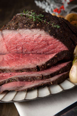 Uncut piece pf peppercorn roast beef with herbed Yorkshire puddings garnished with roasted vegetables.の写真素材