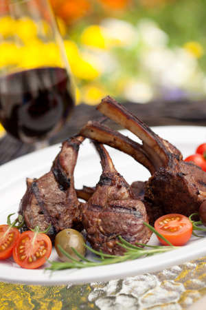 Grilled lamb chops served with cherry tomatoes and olives. Watermelon and wine. Outside dinner in a garden.の写真素材