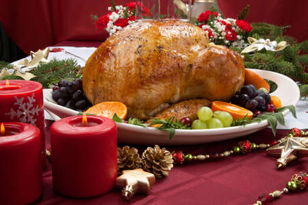 Roasted herb rubbed turkey garnished with fresh grapes, oranges, and cranberry is ready for Christmas dinner. Ornaments, Champagne, candles, and other Christmas decorations on feast table.の写真素材