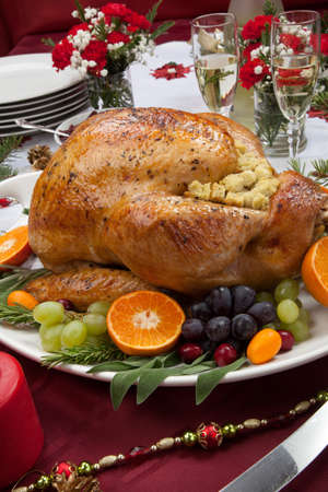 Roasted herb rubbed turkey garnished with fresh grapes, oranges, and cranberry is ready for Christmas dinner. Ornaments, Champagne, candles, and other Christmas decorations on feast table.の写真素材