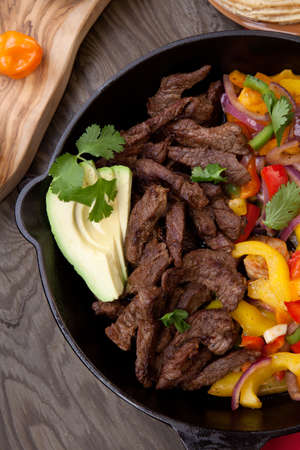 Beef fajitas with bell pepper, onion, and avocado in cast iron skillet ready to be served.の写真素材