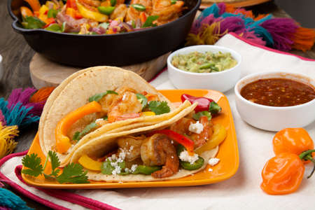 Two shrimp fajitas with bell pepper, onion, and jalapeno in a plate and shrimp fajitas in a cast iron skillet ready to be served. Guacamole, salsa, and tortillas.の写真素材