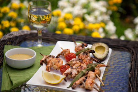 Plate of grilled shrimps skewers with grilled vegetables and avocado. Served with lemon and lemon butter sauce. Outside dinner in a garden.の写真素材