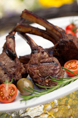 Grilled lamb chops served with cherry tomatoes and olives. Watermelon and wine. Outside dinner in a garden.の写真素材