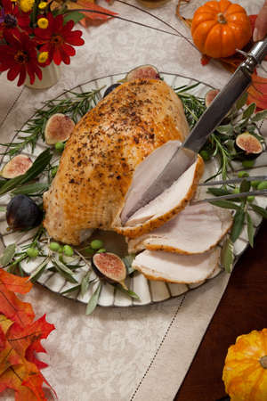 Carving whole roasted turkey breast, Mediterranean style, garnished with fresh figs, olives, and herbs. Surrounded by pumpkins, candles, red wine, and ornaments. Thanksgiving theme.の写真素材