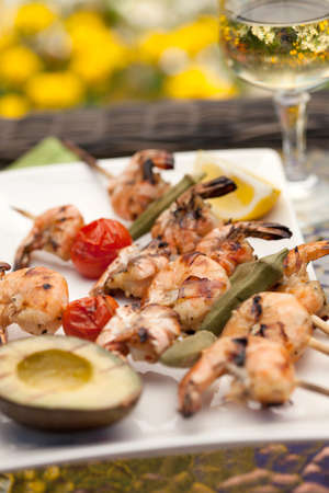Plate of grilled shrimps skewers with grilled vegetables and avocado. Served with lemon and lemon butter sauce. Outside dinner in a garden.の写真素材