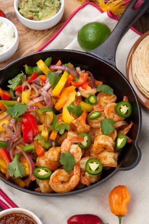 Shrimp fajitas with bell pepper, onion, and jalapeno in cast iron skillet ready to be served. Guacamole, salsa, and tortillas.の写真素材