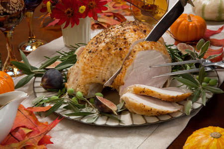 Carving whole roasted turkey breast, Mediterranean style, garnished with fresh figs, olives, and herbs. Surrounded by pumpkins, candles, red wine, and ornaments. Thanksgiving theme.の写真素材