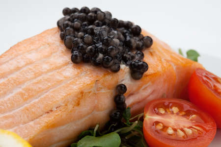 Close up of delicious pan fried salmon with fresh black caviar, tomatoes, and microgreens salad. Elite food.の写真素材