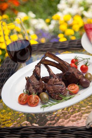 Grilled lamb chops served with cherry tomatoes and olives. Watermelon and wine. Outside dinner in a garden.の写真素材