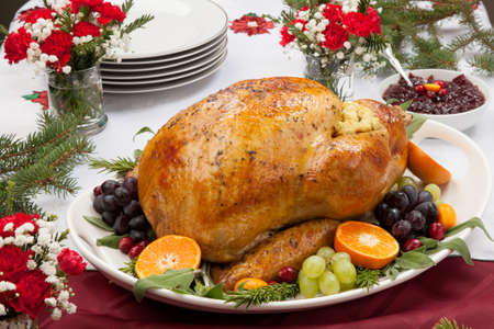 Roasted herb rubbed turkey garnished with fresh grapes, oranges, and cranberry is ready for Christmas dinner. Ornaments, Champagne, candles, and other Christmas decorations on feast table.の写真素材