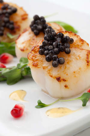 Close up of delicious appetizer scallops with black caviar. Garnished with asparagus, pomegranate seeds, microgreens, and sauce. Elite food.の写真素材