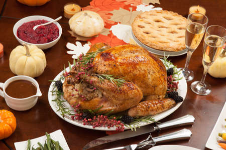 Roasted pepper turkey for Thanksgiving, garnished with pink pepper, blackberry, and fresh rosemary twigs on a dinner tableの写真素材