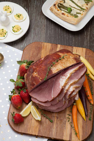 Delicious spicey roasted ham with deviled eggs, asparagus parmesan pastry, butternut squash with green peas, baby carrots, strawberries, and Easter decoration.の写真素材