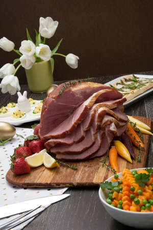 Delicious spicey roasted ham with deviled eggs, asparagus parmesan pastry, butternut squash with green peas, baby carrots, strawberries, and Easter decoration.の写真素材