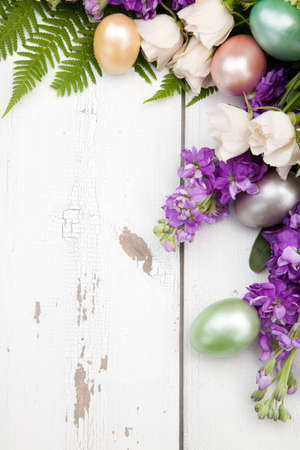 Roses, stock, and hydrangea flowers with easter eggs frame over rustic wooden boards, background for Easter. Copy space.の写真素材