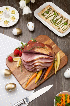 Delicious spicey roasted ham with deviled eggs, asparagus parmesan pastry, butternut squash with green peas, baby carrots, strawberries, and Easter decoration.の写真素材