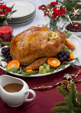 Roasted herb rubbed turkey garnished with fresh grapes, oranges, and cranberry is ready for Christmas dinner. Ornaments, Champagne, candles, and other Christmas decorations on feast table.の写真素材
