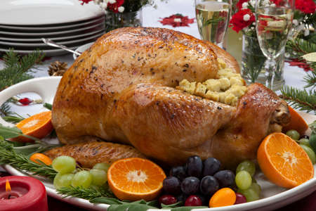 Roasted herb rubbed turkey garnished with fresh grapes, oranges, and cranberry is ready for Christmas dinner. Ornaments, Champagne, candles, and other Christmas decorations on feast table.の写真素材