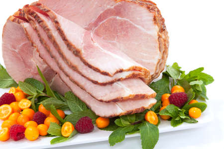 Closeup of delicious roasted sliced ham with fresh mint, kumquat, and raspberries over white backgroundの写真素材