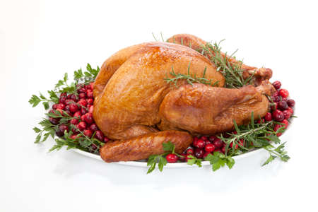 Smoked turkey on a tray garnished with fresh cranberries and herbs over whiteの写真素材