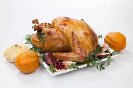 Garnished traditional roasted turkey for Thanksgiving, garnished with fresh figs, pomegranate, and herbs. On white background with pumpkins.の写真素材