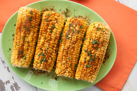 Closeup of Mexican style grilled yellow corn with tortilla chips, beer, and lime wedges. Mexican food.の写真素材