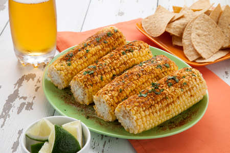 Closeup of Mexican style grilled yellow corn with tortilla chips, beer, and lime wedges. Mexican food.の写真素材