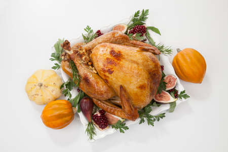 Garnished traditional roasted turkey for Thanksgiving, garnished with fresh figs, pomegranate, and herbs. On white background with pumpkins.の写真素材