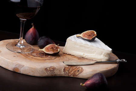 Closeup of Brie cheese with fresh black figs and glass of red wine - great snack for wine tasting. Over black background. Contemporary appetizers series.の写真素材