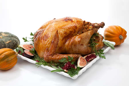 Garnished traditional roasted turkey for Thanksgiving, garnished with fresh figs, pomegranate, and herbs. On white background with pumpkins.の写真素材