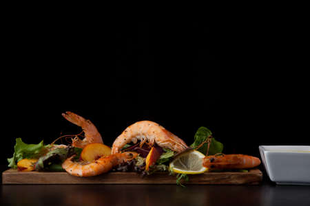 Close up of delicious savory whole shrimp salad with fresh nectarine, green lettuce, and lemon. Mustard sauce. Over black background. Contemporary appetizers series.の写真素材