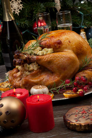 Rustic style roasted Christmas turkey garnished with roasted garlic, lemon, and rosehips. Surrounded with rustic Christmas ornaments, candles, wine, flowers, and Christmas tree in the background.の写真素材