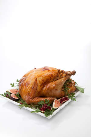 Garnished traditional roasted turkey, garnished with fresh figs, pomegranate, and herbs. On white background.の写真素材