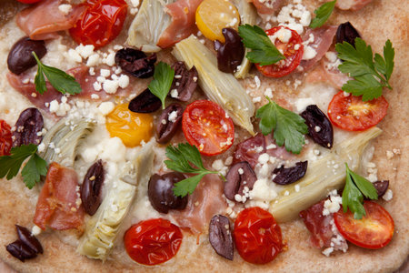 Closeup of home made Mediterranean flatbread made with prosciutto, artichoke, cherry tomatoes, feta...