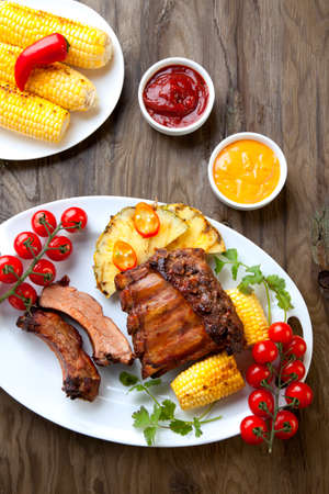 Grilled pork ribs, corn, and pineapple with chili pepper, cherry tomatoes, and sauces.の写真素材