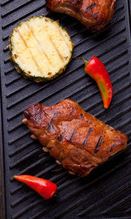 Grilled pork ribs on griddle with chili pepper and grilled pineapple.の写真素材