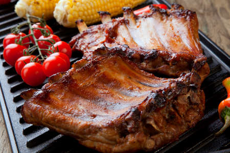 Grilled pork ribs on griddle with chili pepper, cherry tomatoes, and grilled cornの写真素材
