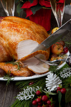 Carving garnished roasted Christmas turkey with grab apples, sweet chestnut, cranberry, Christmas ornaments, candles, and pine cones.の写真素材