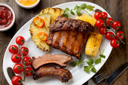 Grilled pork ribs, corn, and pineapple with chili pepper, cherry tomatoes, and sauces.の写真素材